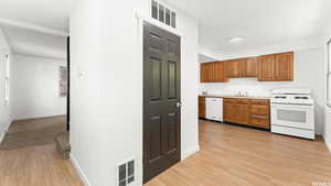 Kitchen featuring white appliances, light wood-type flooring, light countertops, and brown cabinetry