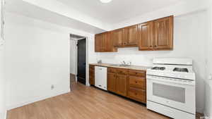 Kitchen featuring white appliances, brown cabinets, light countertops, and light wood-style flooring