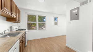 Kitchen with white appliances, brown cabinetry, electric panel, and light wood-style flooring