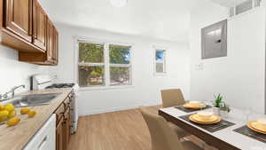 Kitchen with white appliances, brown cabinetry, light wood-style flooring, and electric panel