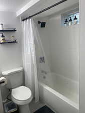 Full bath featuring a textured ceiling, shower / tub combo with curtain, and a textured wall