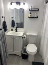 Full bath with a textured wall, vanity, light wood-style floors, and curtained shower