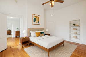 Bedroom with light wood-style floors, arched walkways, ceiling fan, and a high ceiling