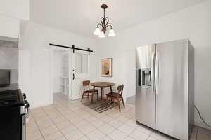 Kitchen featuring appliances with stainless steel finishes, a barn door, a chandelier, hanging light fixtures, and light tile patterned flooring
