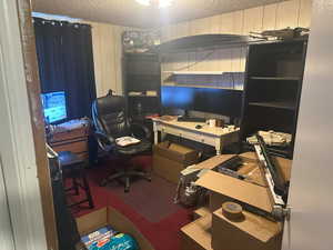 Carpeted home office with a textured ceiling and wood walls