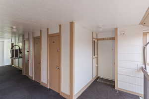 Corridor featuring a textured ceiling and dark carpet