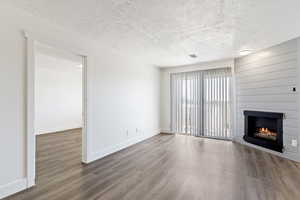 Unfurnished living room featuring a textured ceiling, dark wood-style floors, and a fireplace