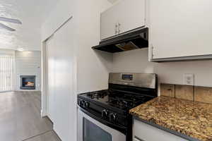 Kitchen featuring stainless steel gas range, a textured ceiling, under cabinet range hood, a fireplace, and light wood-type flooring