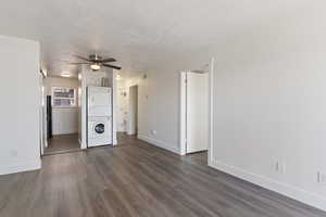 Unfurnished living room featuring a textured ceiling, dark wood-style flooring, a ceiling fan, and stacked washer and clothes dryer