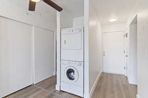 Washroom with light wood finished floors, estacked washer and dryer, a textured ceiling, and ceiling fan