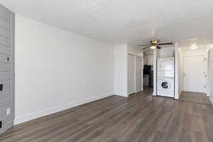 Unfurnished living room featuring dark wood-style flooring, a textured ceiling, estacked washer and dryer, and ceiling fan