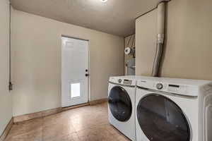 Laundry room with a textured ceiling, washing machine and dryer, light tile patterned floors, and strapped water heater