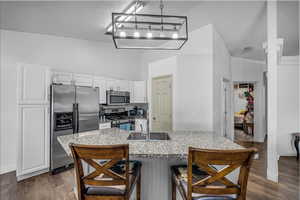 Kitchen featuring stainless steel appliances, a breakfast bar, light stone countertops, white cabinetry, and dark wood-style floors