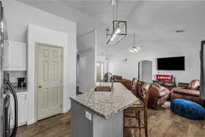 Kitchen with light stone counters, lofted ceiling, decorative light fixtures, a kitchen island with sink, and a kitchen breakfast bar