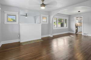 Unfurnished living room with dark wood-style flooring, a ceiling fan, and arched walkways