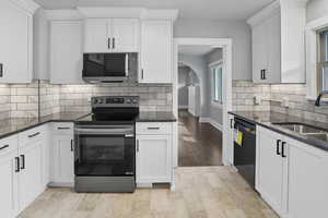 Kitchen with decorative backsplash, stainless steel appliances, arched walkways, dark stone counters, and white cabinetry