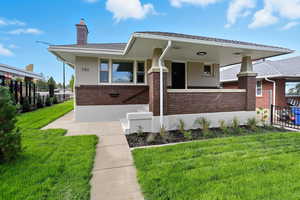 View of front facade with brick siding, a chimney, a porch, and stucco siding