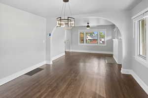 Unfurnished dining area with arched walkways, dark wood-type flooring, a chandelier, and ceiling fan