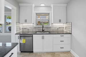 Kitchen with dark stone counters, white cabinets, dishwasher, and tasteful backsplash