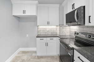Kitchen featuring electric range oven, black microwave, backsplash, white cabinetry, and dark stone countertops
