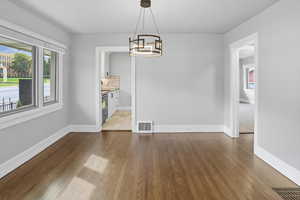 Unfurnished dining area with healthy amount of natural light, dark wood-style flooring, and a chandelier