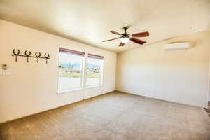 Empty room featuring vaulted ceiling, carpet, a ceiling fan, and a wall mounted air conditioner