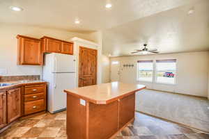 Kitchen with brown cabinets, freestanding refrigerator, vaulted ceiling, a center island, and light countertops