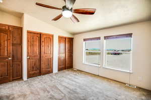 Unfurnished bedroom featuring two closets, carpet floors, vaulted ceiling, a ceiling fan, and a textured ceiling