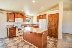 Kitchen featuring vaulted ceiling, white appliances, brown cabinets, light countertops, and recessed lighting