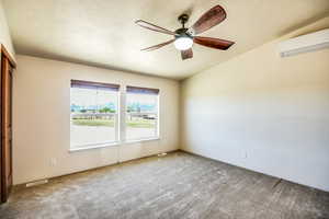 Empty room featuring carpet flooring, a wall mounted AC, and a ceiling fan