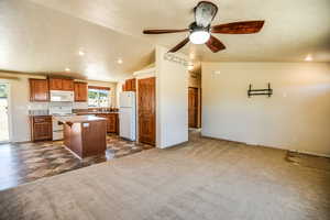 Kitchen with dark carpet, brown cabinetry, lofted ceiling, white appliances, and a kitchen breakfast bar