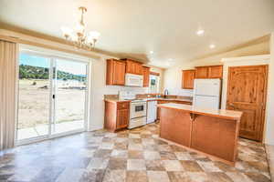 Kitchen with light countertops, white appliances, brown cabinetry, pendant lighting, and vaulted ceiling