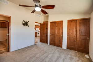 Unfurnished bedroom with lofted ceiling, multiple closets, light colored carpet, and a ceiling fan