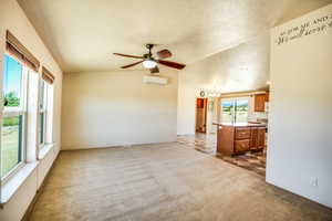 Unfurnished living room featuring dark colored carpet, a chandelier, ceiling fan, and vaulted ceiling