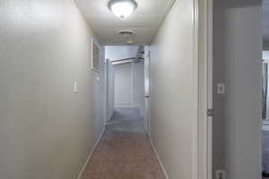 Hallway with light colored carpet and a textured wall