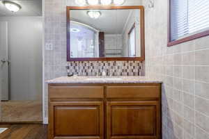 Bathroom featuring vanity, decorative backsplash, and dark wood-style flooring