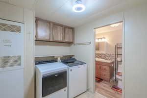 Washroom featuring a heating unit, washer and clothes dryer, cabinet space, and light wood-style flooring
