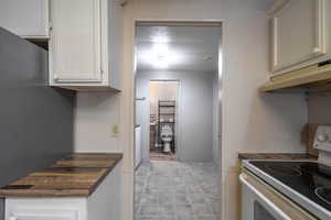 Kitchen featuring electric stove, butcher block countertops, and white cabinetry