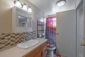 Full bathroom with vanity, decorative backsplash, a shower with curtain, a textured ceiling, and dark wood-style flooring