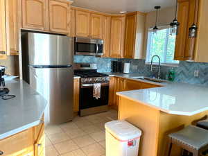 Kitchen featuring appliances with stainless steel finishes, light tile patterned floors, tasteful backsplash, a peninsula, and light stone countertops
