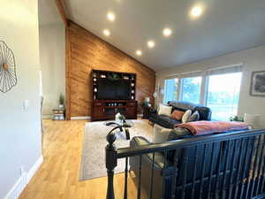 Living area featuring wooden walls, light wood-style flooring, high vaulted ceiling, and recessed lighting