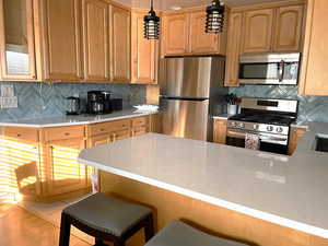 Kitchen featuring appliances with stainless steel finishes, tasteful backsplash, a peninsula, and light stone counters