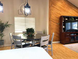 Dining room featuring wood walls, light wood-type flooring, healthy amount of natural light, a chandelier, and a high ceiling