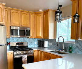 Kitchen with tasteful backsplash, appliances with stainless steel finishes, light stone counters, and hanging light fixtures