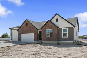 View of front facade with board and batten siding, an attached garage, concrete driveway, a shingled roof, and brick siding