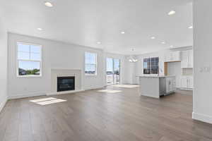 Unfurnished living room with recessed lighting, a chandelier, a glass covered fireplace, and light wood-type flooring
