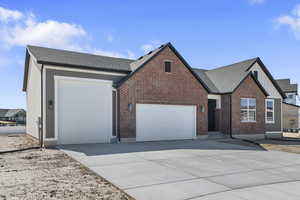 View of front of home with board and batten siding, an attached garage, concrete driveway, and brick siding