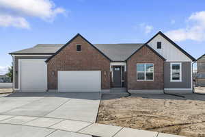 View of front of home with board and batten siding, a shingled roof, a garage, concrete driveway, and brick siding