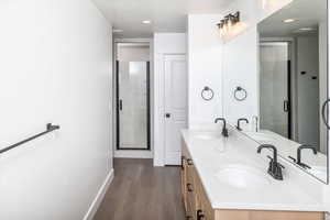 Bathroom featuring dark wood-type flooring, double vanity, a textured ceiling, a stall shower, and recessed lighting