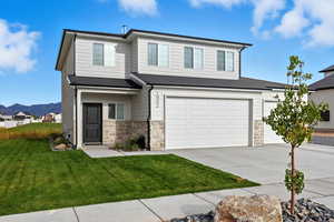 View of front of property featuring stone siding, concrete driveway, a front lawn, and a mountain view